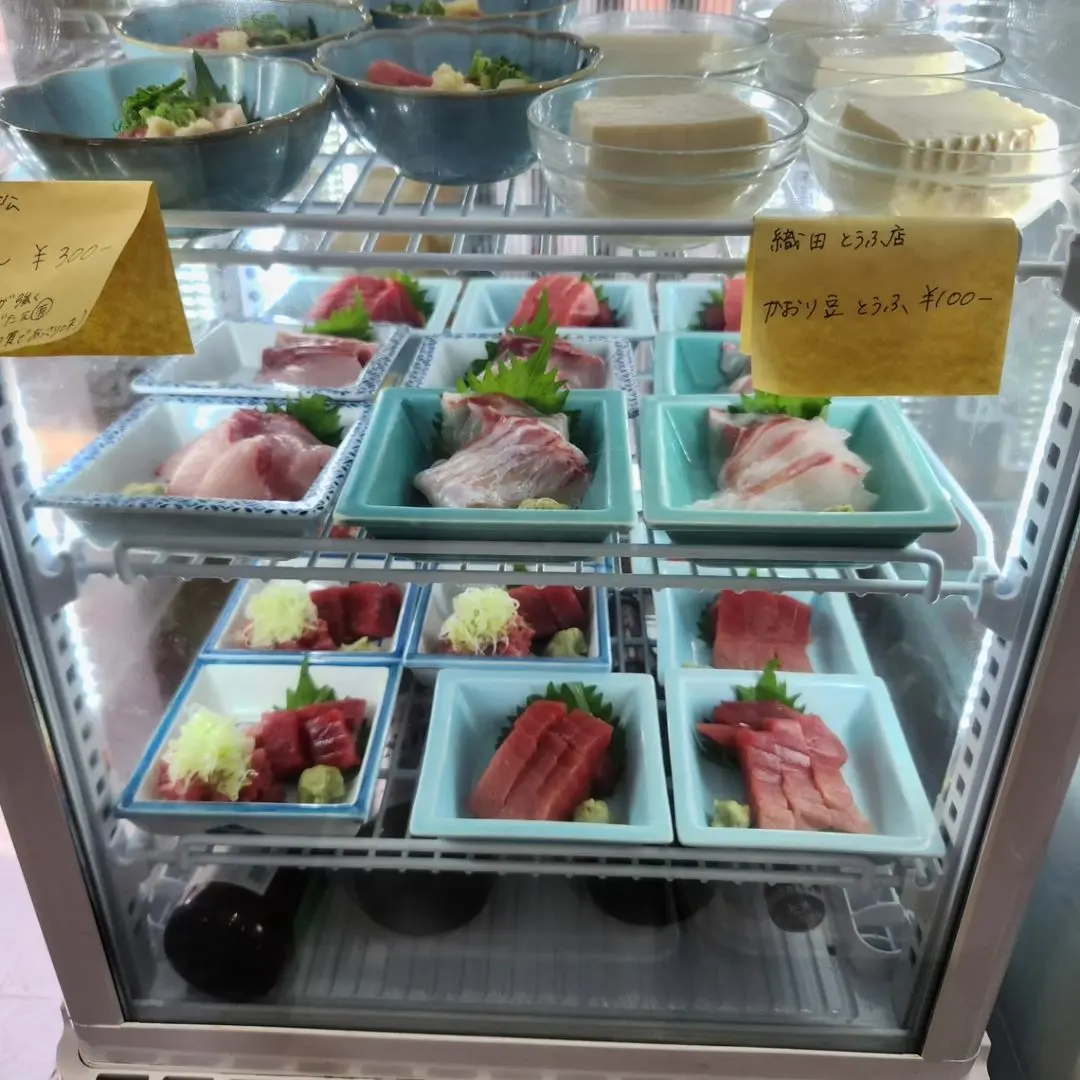 The refrigerated display case features fresh sashimi and other delicacies.