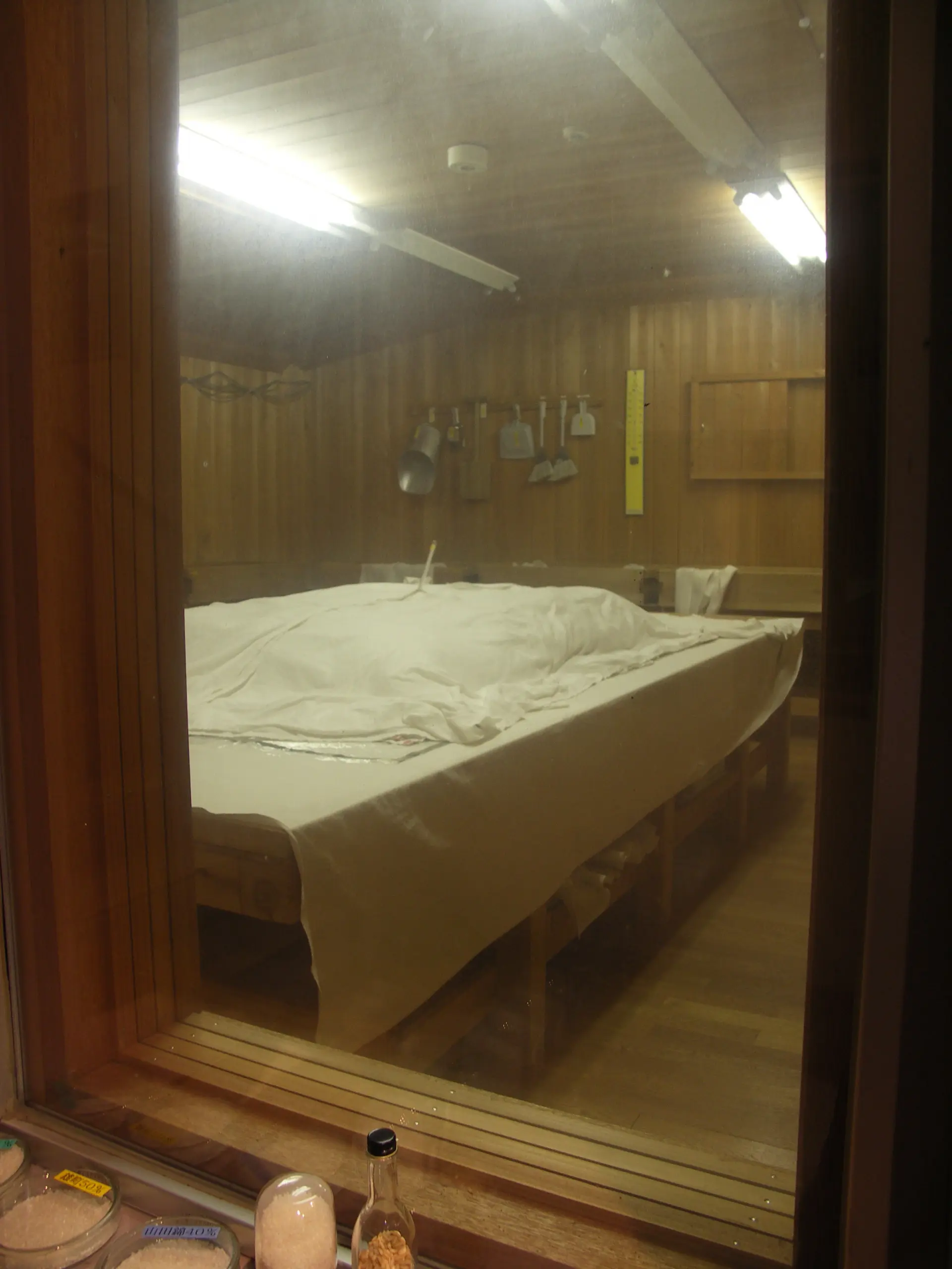 The sake brewing process can be observed through glass panels. The photo shows the koji room, where steamed rice is inoculated with koji mold.